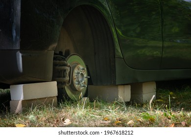 Close Up Of Car On Bricks Outside. Concept Of Stolen Vehicle Wheels. Car With Missing Wheel.