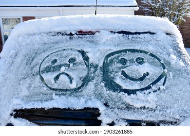 close up car screen covered in snow and two emoji faces drawn into ice  one happy   one sad  outside cold sunny winter's day