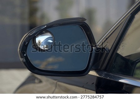Close up of a car side mirror with installed blind spot mirror and rain guard visor, automotive safety and weather protection accessories