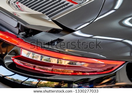 Close up of car taillight & aerodynamic design of modern luxury sportscar with reflection on black paint after wash & wax. Shiny supercar. Concept of car detailing and paint protection background