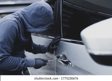 Close up car thief hand holding screwdriver tamper yank and glove black stealing automobile trying door handle to see if vehicle is unlocked  trying to break into inside. 