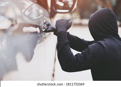 Close up car thief hand holding screwdriver tamper yank and glove black stealing automobile trying door handle to see if vehicle is unlocked  trying to break into inside. 