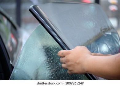 Close Up Of Car Window Tint Installation. Ceramic Film Provide Heat Rejection & UV Protection. Automotive Film Installed To Car Glass Surface. Professional Tinting Service Background. Hand Moving