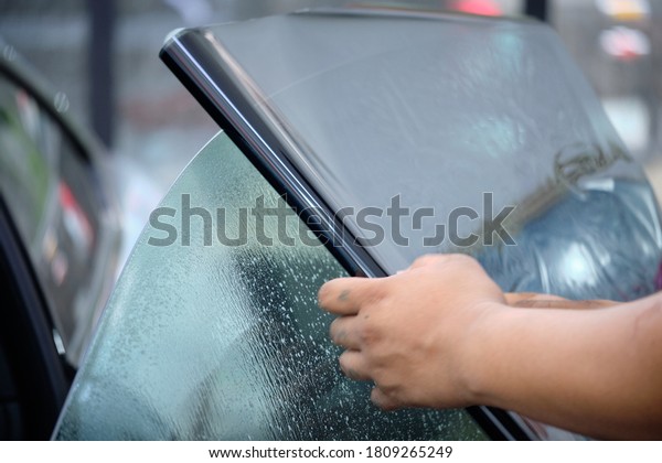 Close up of car window tint installation. Ceramic\
film provide heat rejection & UV protection. Automotive film\
installed to car glass surface. Professional tinting service\
background. Hand moving