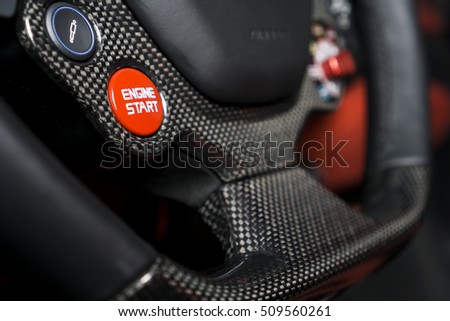 Close up carbon fibre steering wheel with red start stop engine button, super sport car