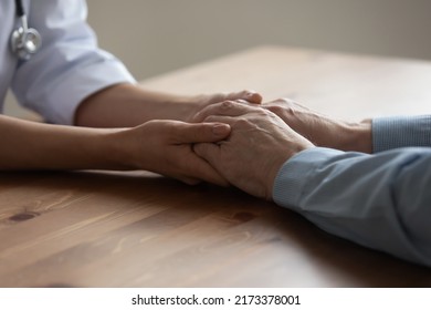 Close up caregiver comforting aged old patient, sitting at desk in hospital, caring woman doctor nurse holding senior mature man hands, expressing empathy and support, psychological help concept - Shutterstock ID 2173378001