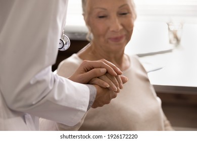 Close up caregiver holding mature woman hand, caring doctor nurse wearing uniform comforting and supporting unhealthy senior patient, expressing empathy, professional psychological help concept