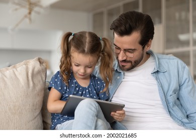 Close Up Caring Father With Little Daughter Using Modern Tablet Together, Sitting On Cozy Couch At Home, Dad Wearing Glasses And Adorable Preschool Girl Child Looking At Device Screen, Playing Game