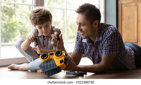 Close up caring father and little son fixing toy car, lying on warm wooden floor at home, smiling young dad and cute adorable boy using screwdriver, having fun, spending leisure time together