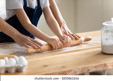 Close Up Caring Mother And Little Daughter Wearing Aprons Rolling Out Dough Together, Working With Rolling Pin, Standing At Wooden Countertop In Kitchen, Family Cooking Baking Together