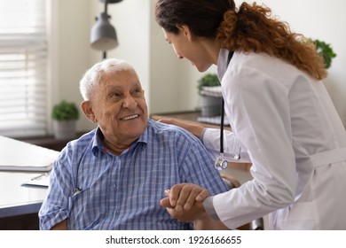 Close up caring nurse holding smiling mature patient hand at meeting in hospital, doctor caregiver wearing uniform comforting and supporting senior man, good news about treatment, empathy and care