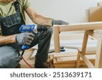 Close up of carpenter drilling a board with a screwdriver. Professional woodworker using tools for work in his workshop. Small business concept.