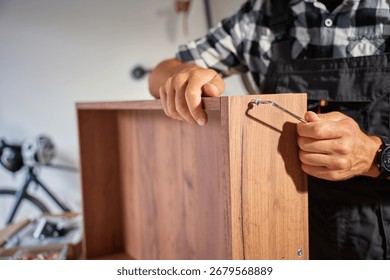 Close up of carpenter using Allen key while assembling wooden furniture in workshop. Man using hex key to tighten screws. Concept of carpentry and furniture making
