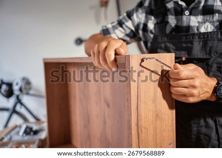 Close up of carpenter using Allen key while assembling wooden furniture in workshop. Man using hex key to tighten screws. Concept of carpentry and furniture making
