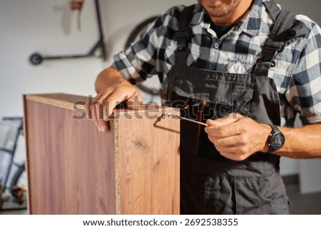 Close up of carpenter using Allen key while assembling wooden furniture in workshop. Man using hex key to tighten screws. Concept of carpentry and furniture making