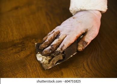 Close up of a carpenter wearing protective gloves, applying varnish onto a wooden surface with a cloth