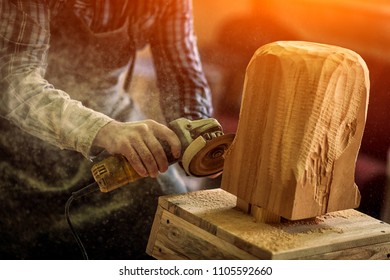 Close up of a  carpenter in work clothes and small buiness owner working in woodwork workshop, processes the board with an angle grinder , on the table is a hammer and many tools 
