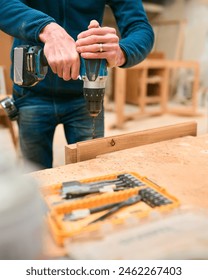 Close Up Of Carpenter At Workbench In Workshop Using Cordless Electric Drill