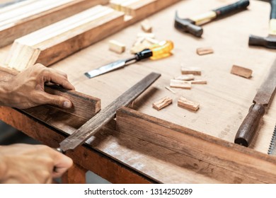 Close up of carpenter working on a piece of wood using a rasp to smooth it with others tool like hammer and chisel on the table