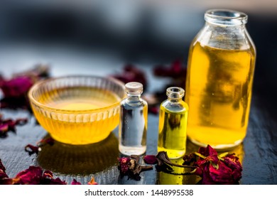 Close Up Of Castor Oil, Tea Tree Oil, And Some Coconut Oil In Bottles On The Wooden Surface Along With Some Raw Honey And Rose Petals Also Present On The Surface.