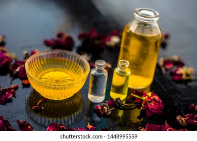 Close Up Of Castor Oil, Tea Tree Oil, And Some Coconut Oil In Bottles On The Wooden Surface Along With Some Raw Honey And Rose Petals Also Present On The Surface.