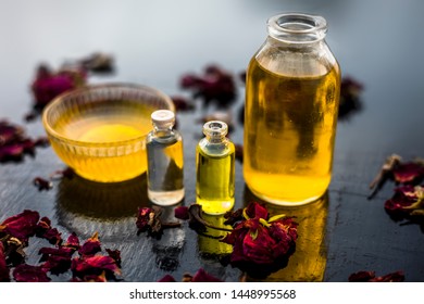 Close Up Of Castor Oil, Tea Tree Oil, And Some Coconut Oil In Bottles On The Wooden Surface Along With Some Raw Honey And Rose Petals Also Present On The Surface.