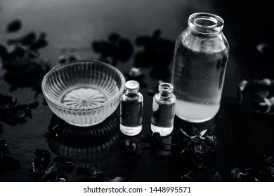 Close Up Of Castor Oil, Tea Tree Oil, And Some Coconut Oil In Bottles On The Wooden Surface Along With Some Raw Honey And Rose Petals Also Present On The Surface.