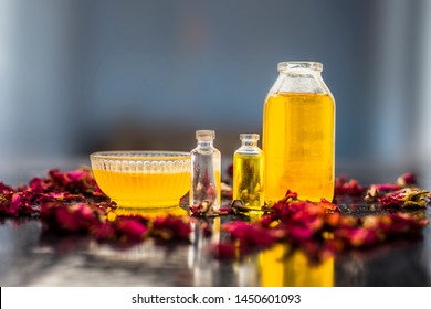 Close Up Of Castor Oil, Tea Tree Oil, And Some Coconut Oil In Bottles On The Wooden Surface Along With Some Raw Honey And Rose Petals Also Present On The Surface.