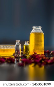 Close Up Of Castor Oil, Tea Tree Oil, And Some Coconut Oil In Bottles On The Wooden Surface Along With Some Raw Honey And Rose Petals Also Present On The Surface.