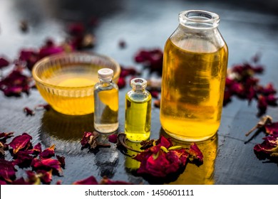 Close Up Of Castor Oil, Tea Tree Oil, And Some Coconut Oil In Bottles On The Wooden Surface Along With Some Raw Honey And Rose Petals Also Present On The Surface.