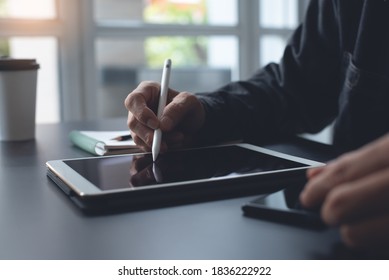 Close up of casual business man hand using stylus pen touching on digital tablet, working at modern home office. Graphic designer creating his design project on wooden table via internet mobile apps - Shutterstock ID 1836222922
