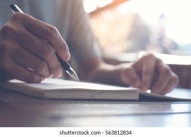 Close up of casual man writing on paper notebook or old diary at home