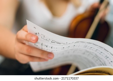close up Caucasian female hand turning page of sheet music on music stand, woman violinist blurred in background, with copy space.