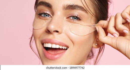 Close Up Of Caucasian Girl With Natural No Makeup Look And White Smile, Take Off Silicone Under Eye Patches And Smiling Happy, Using Skincare Products From Dark Circles, Pink Background.