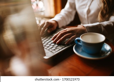 Close up of  a caucasian  girl typing on a keyboard lap top next to a cup of coffee