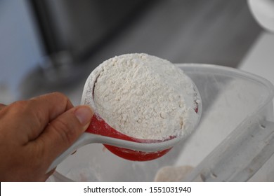 close up of caucasian hand  holding a red and white plastic measuring cup full of flour dumping into a mixing bowl with other ingredients - Shutterstock ID 1551031940