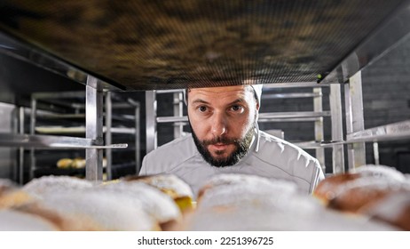 Close up of Caucasian handsome male baker in hat looking and smelling just-baked bread. Bakery business concept. Man working in bakehouse and checking baguettes or rolls. Pastry. Work in food selling. - Shutterstock ID 2251396725