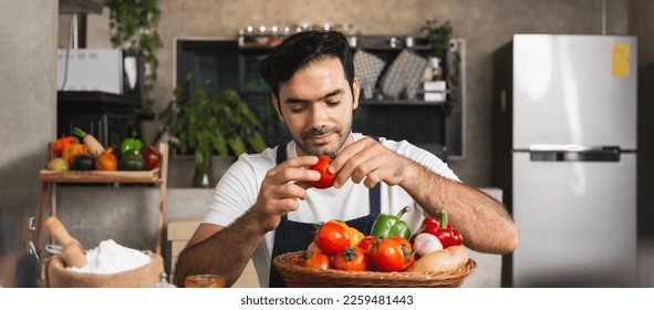 Close up Caucasian man wearing apron hand holding fresh organic vegetable tomato bell pepper potato garlic onion basket on wooden table in home kitchen. Young man chef select good quality ingredient. - Powered by Shutterstock