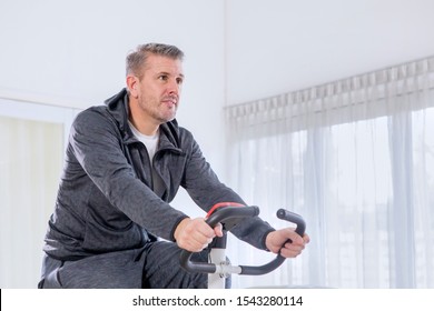 Close Up Of Caucasian Man Wearing Sportswear While Exercising On A Spin Bike In The Living Room. Shot At Home