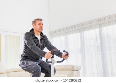 Close Up Of Caucasian Man Wearing Sportswear While Sitting On A Spin Bike In The Living Room. Shot At Home