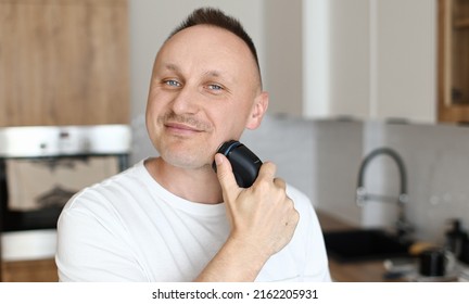 close up of caucasian man in white t shirt is shaving beard with electric razor at bathroom at home. copy space. mans beauty concept. morning routine. - Powered by Shutterstock