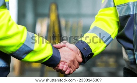 Close up of Caucasian men shaking hands at factory as sign of agreement and good work together. Inside. Males constructors or builders shake hands. Gesture of agreeing of two workmen at manufactory.