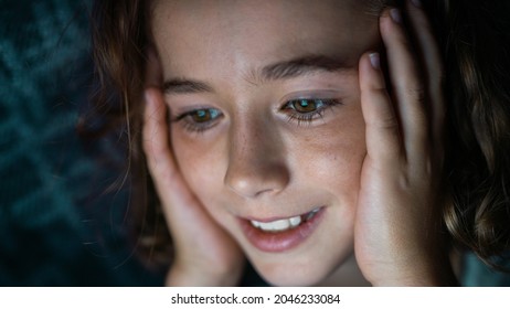 Close Up Of A Caucasian School Kid With Curly Hair And Brown Eyes Under The Blue Blanket Looking Happy And Excited, Watching A Movie On The Tablet, While Being Home Schooled.