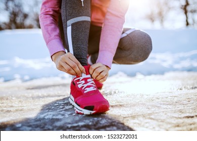 Close Up Of Caucasian Sporty Woman Crouching Outdoors In Sportswear And Tying Shoelace. Winter Fitness Concept.