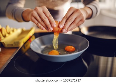 Close Up Of Caucasian Woman Breaking Egg And Making Sunny Side Up Eggs. Domestic Kitchen Interior. Breakfast Preparation.