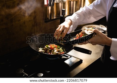 Close up of a Caucasian woman at a cookery class, putting vegetables on a frying pan. Active Seniors enjoying their retirement.