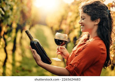 Close up  of the caucasian woman holding glass and bottle of red wine .Sommelier tasting wine outdoors during sunset. - Powered by Shutterstock