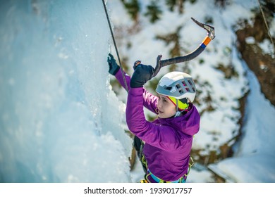 Close up of a Caucasian woman with ice climbing equipment, hiking at a frozen waterfall, swinging the ice axe