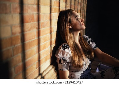 Close Up Of Caucasian Woman Sitting On The Ground Enjoying The Feeling Of The Warmth Of The Sun On Her Face Coming In From Outside