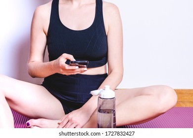 close up of caucasian woman wearing black fitness clothing resting from exercise and using her phone